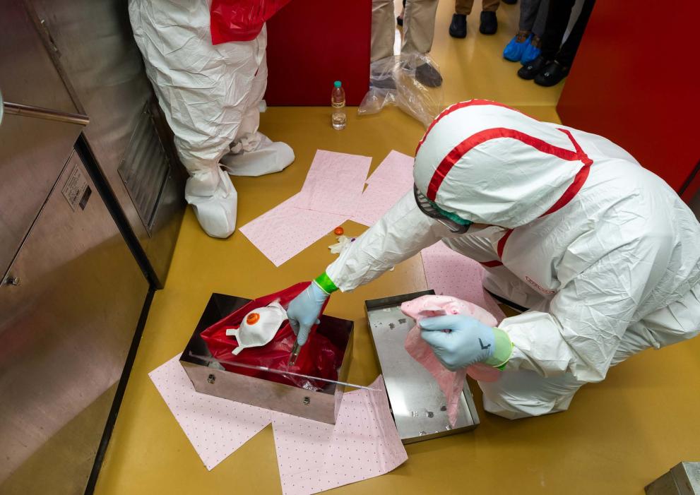 Two CBRN practitioners wearing protective gear place CBRN waste in a box.