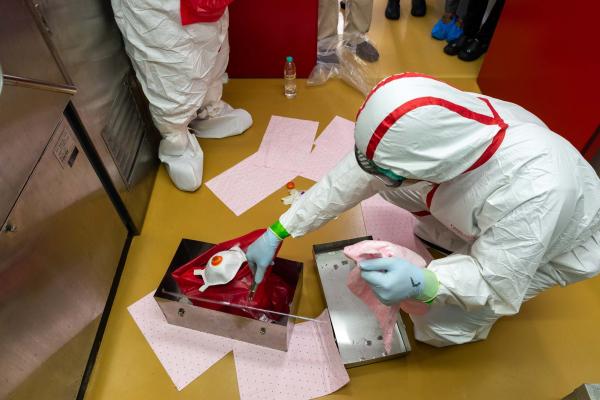 Two CBRN practitioners wearing protective gear place CBRN waste in a box.